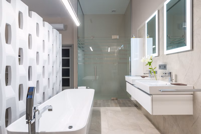 White bathtub with tap near decorative partition placed near sink and mirrors in stylish light bathroom with glass shower cabin